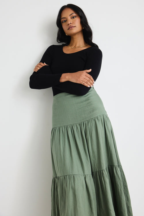 Model wears a khaki maxi skirt and black long sleeve top