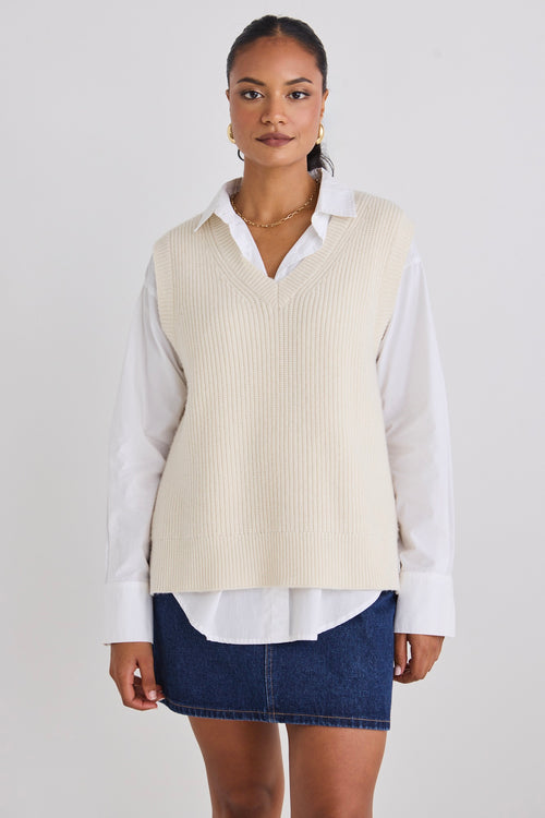 Model wears a knit vest with a white shirt 