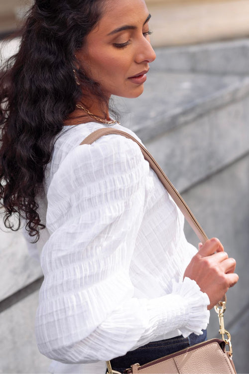model wears a white cotton long sleeve top with blue jeans and a brown handbag