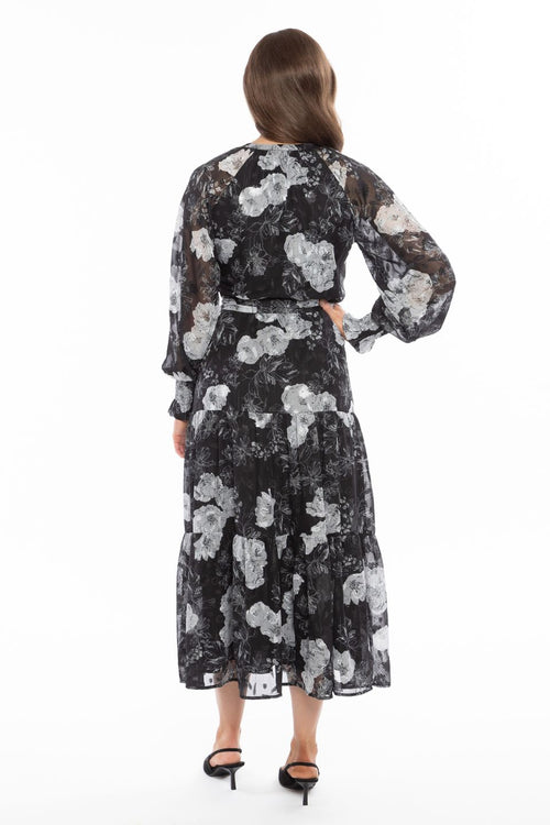 Model wearing long black and white floral maxi dress with black heels