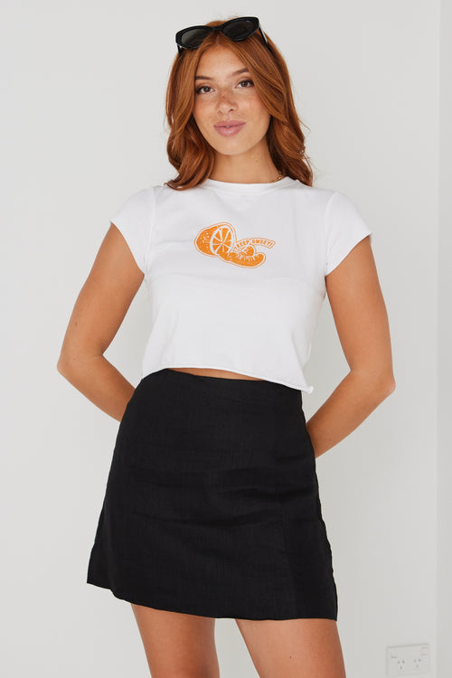 model wearing white crop top tee with an orange on the front and a black skirt