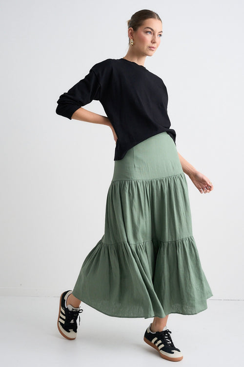 Model wears a khaki maxi skirt and black long sleeve top